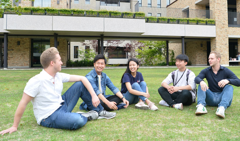 国籍の様々な学生5人が芝生の上で談笑しているイメージ